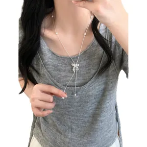 Elegant silver-tone hollow bow pendant necklace with zircons and pearls worn by a model