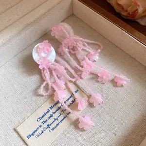 Close-up of elegant pink resin flower tassel earrings displayed in a cream jewelry box