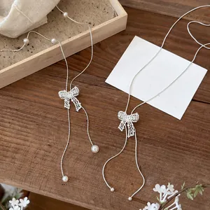 Detail of elegant silver hollow bow pendant necklace with pearls on wood background
