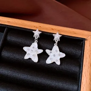 Macro view of elegant silver star drop earrings featuring mother of pearl inlay and crystals