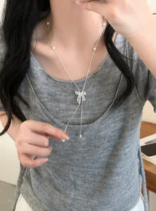 Model wearing a zircon hollow bow pendant necklace with pearl accents on grey top.