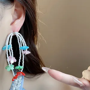 Close-up detail of colorful resin flower and white bead tassel earrings worn by a model