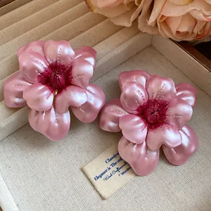 Französische Vintage-Blumenohrstecker aus rosa Metall auf einem strukturierten Tablett