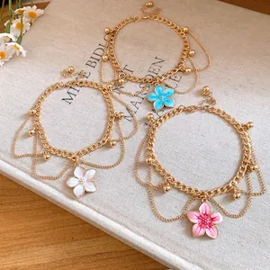 Set of gold anklets with colorful enamel flower charms and delicate chain layers.