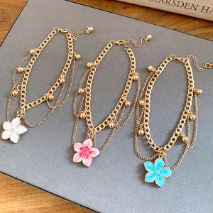 Detailed view of gold-toned layered anklets with colorful enamel flower charms