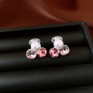 Dettaglio macro di orecchini a clip con perla bianca e cristalli rosa lucidi.