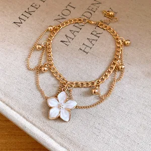 Close-up of gold layered anklet with white enamel flower charm and bead details