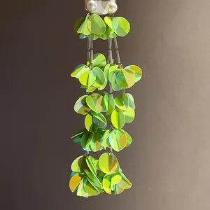Dettaglio di orecchini a nappa con paillettes verde lime e perle a bottone