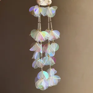 Dettaglio di lunghi orecchini a nappa cangianti con paillettes olografiche effetto conchiglia.