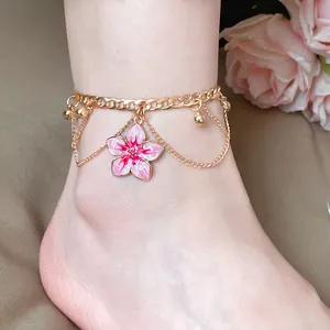Close-up of a gold-tone anklet featuring a pink enamel flower pendant and sphere charms.