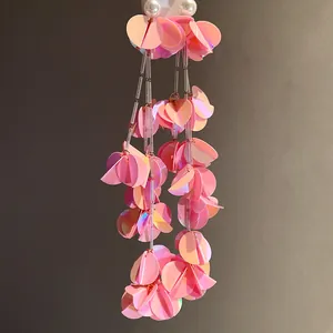 Dettaglio ravvicinato di orecchini a nappa con paillettes rosa iridescenti e perle