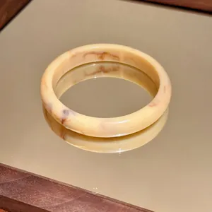 Dettaglio di un bracciale rigido in acrilico marmorizzato crema su uno specchio dorato