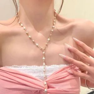 Close-up view of a delicate gold pearl lariat necklace worn by a model in pink clothing