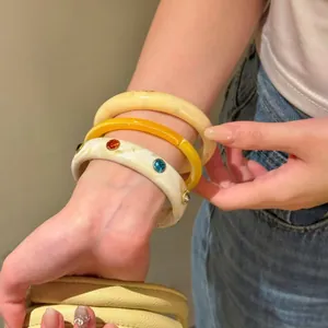 Primo piano di tre braccialetti in resina impilati con strass indossati al polso