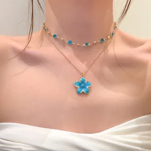 Detailed view of a layered golden necklace with sweet blue flower pendant on a model's neck