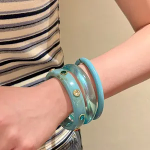 Vista dettagliata di bracciali rigidi in acrilico blu con strass indossati sul polso