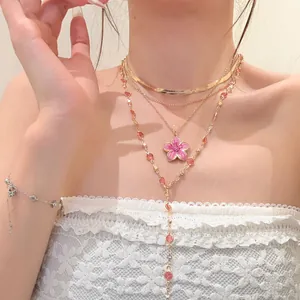 Close-up of layered gold necklaces with a pink enamel flower pendant and beaded chains.