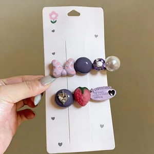 Set of two decorative alligator hair clips with strawberry and bow designs on a card