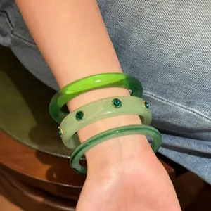 Primo piano di tre braccialetti impilati in resina verde con strass indossati al polso.
