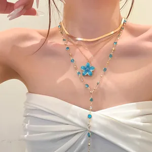 Detailed macro shot of layered gold necklaces with blue flower pendant and rhinestone accents