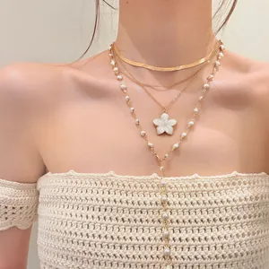 Close-up of layered gold flower and pearl necklace worn on model for vacation style.