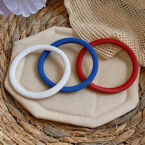 Gros plan de bracelets chaîne à ressort rouge, blanc et bleu sur un coussinet en tissu