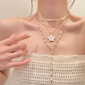 Close-up of three layered gold necklaces with white flower and pearl details