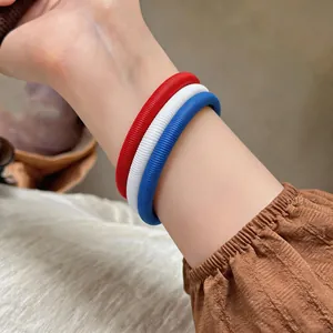 Détail de bracelets à ressort en spirale rouges, blancs et bleus portés au poignet.