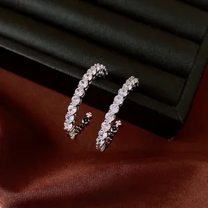 Eleganti orecchini a cerchio a C in argento con zirconi su uno sfondo di raso di lusso