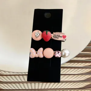 Close-up view of cute hair clips with strawberry, polka dot bow, and pearl on display card
