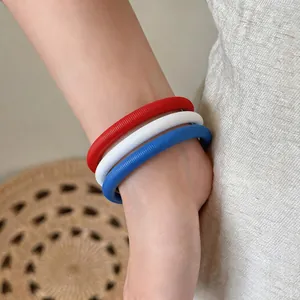 Gros plan de bracelets chaînes à ressort minimalistes en rouge, blanc et bleu sur un poignet.