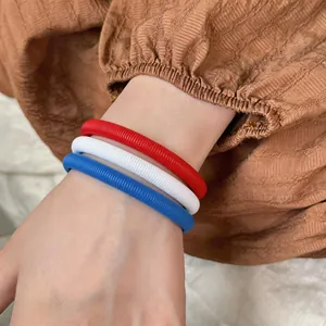 Détail de bracelets à ressort rouges, blancs et bleus portés au poignet sur un vêtement brun.