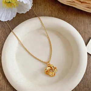 Gros plan d'un collier pendentif fleur nouée vintage doré sur une assiette blanche