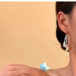 Macro view of Bohemian style drop earrings featuring white shells and blue beads for a vacation look.