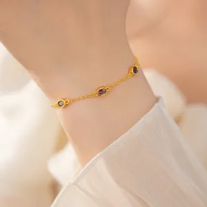 Detaillierte Nahaufnahme eines eleganten Goldarmbands mit drei ovalen lila Edelsteinen am Handgelenk