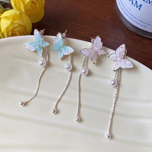 Elegant butterfly tassel stud earrings with pearls in blue and pink, shown on a cream plate