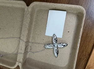 Close-up detail of a silver cross necklace featuring quilted texture and zircons