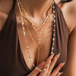 Dettaglio di un set di 5 collane dorate con perle finte e ciondolo a croce con strass.