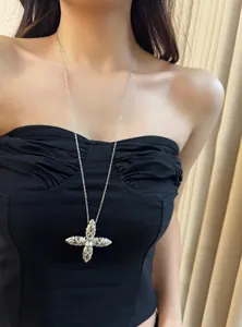 Close-up view of a silver cross pendant necklace with central zircon worn over black top
