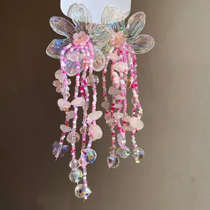 Dettaglio di orecchini a fiore cangianti con nappe di perline rosa e cristalli.