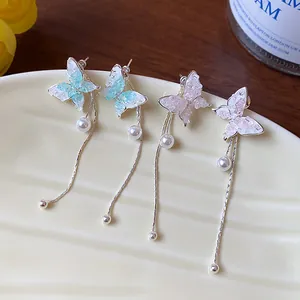 Macro detail of elegant butterfly tassel earrings with pearls on a cream ceramic dish.