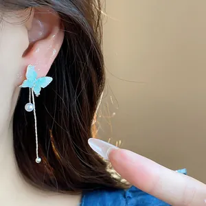 Silver needle earrings featuring a blue glass butterfly and pearl tassel chains