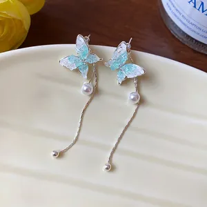 Close-up detail of elegant butterfly tassel earrings with blue crystals and white pearls.