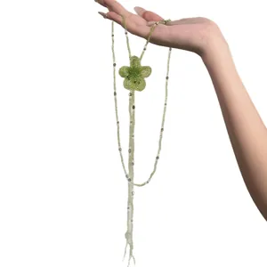 Handmade green beaded flower necklace with long fringe held against white backdrop