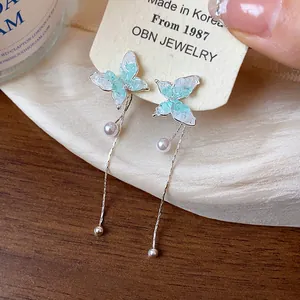 Close-up of butterfly stud earrings with glass wings and long pearl tassels.