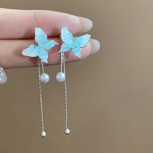 Macro detail of blue butterfly tassel earrings with delicate pearls and silver finish