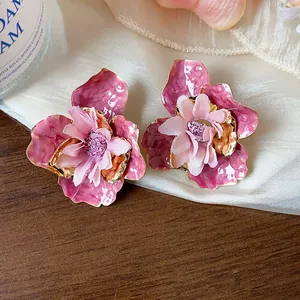 Dettaglio dei orecchini a fiore in smalto rosa con petali di stoffa su tessuto