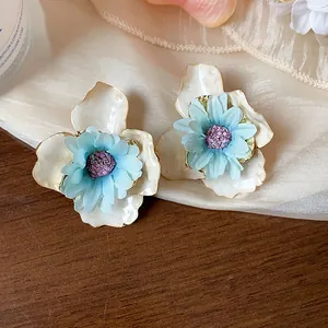 Dettaglio di orecchini a fiore in tessuto con petali di smalto bianco e centro blu