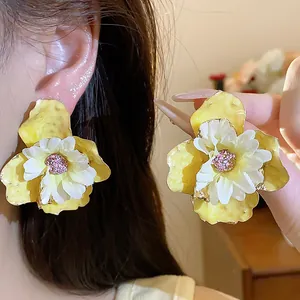 Dettaglio di orecchini a fiore in smalto giallo e tessuto bianco con perni in argento da donna