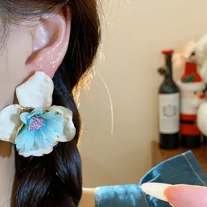 Primo piano di un grande orecchino a lobo a forma di fiore blu e bianco su una modella